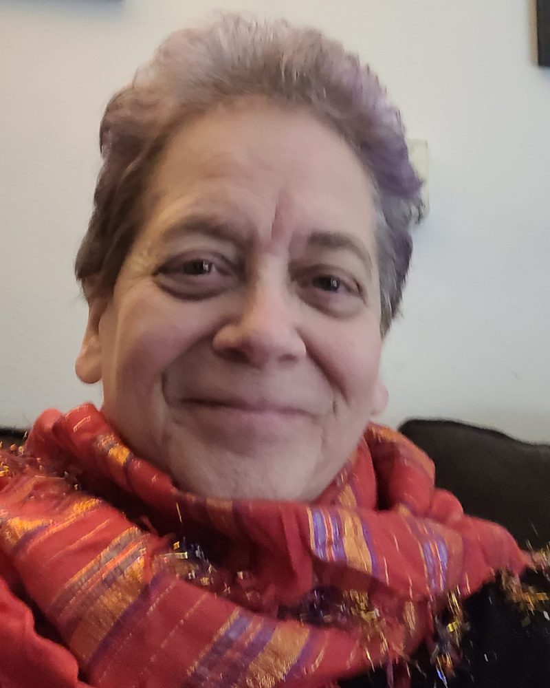 Jo Gustafson, smiling, with purple hair and a red and orange scarf.